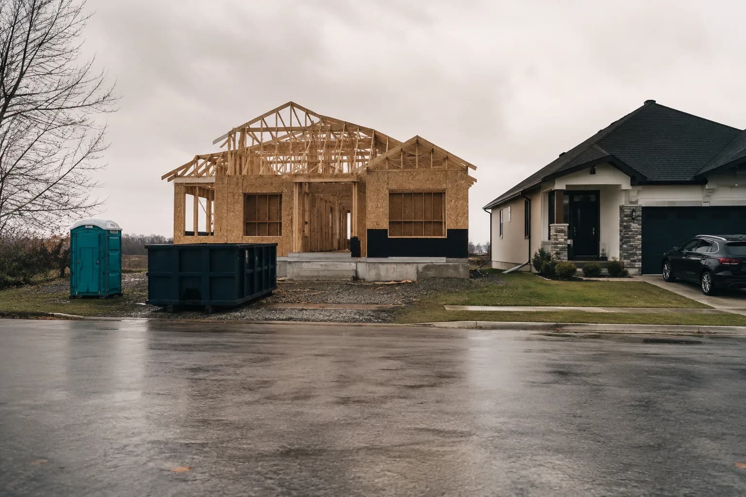 A house frame under construction beside a finished neighbouring house, overcast sky